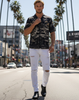 Man walking on a city street wearing a patterned shirt and white pants.