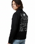 Person wearing a black jacket with white graphics on the back, standing indoors.