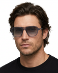 Male model with shaggy dark hair wearing Garrett Leight DOC sunglasses with Pacific Blue frames and Rain Gradient lenses on a white background