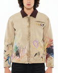 Male wearing a beige jacket with paint splatters in different colors one the lower half.  Brown collar.
