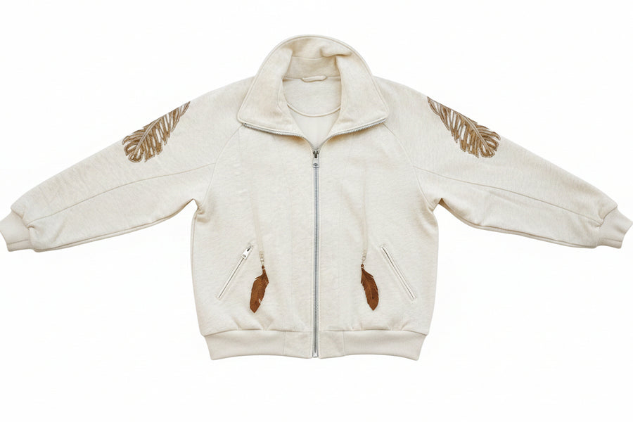 A person wearing a beige 'SLASHED FEATHER' blouson with leather feathers on the hood and sleeves, paired with blue jeans.