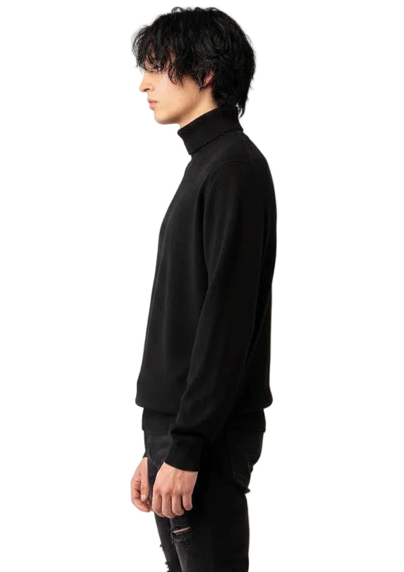 A model with black wavy hair is shown in profile wearing a black turtleneck sweater and black distressed jeans, against a plain white studio background.