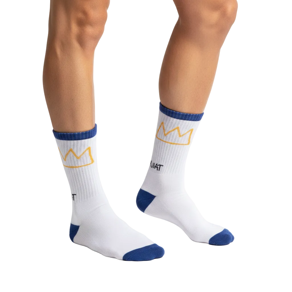 Model wearing Rome Pays Off Basquiat "Crown" crew socks in white with gold crown motifs and blue cuffs, heels, and toes.