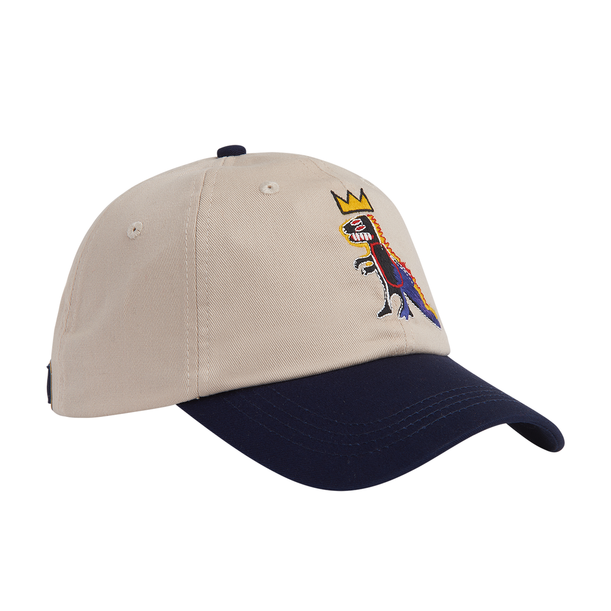 A baseball cap with a beige crown and a dark navy blue visor, featuring an embroidered multicolor graphic of a crowned dinosaur on the front.