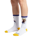 A pair of white crew socks with yellow toes and heels, purple cuffs, and a colorful cartoon graphic on the upper right sock. The brand name 'BROOKS' is printed in black on the sole of the front sock.