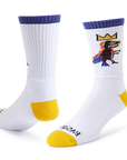 A pair of white crew socks with yellow toes and heels, purple cuffs, and a colorful cartoon graphic on the upper right sock. The brand name 'BROOKS' is printed in black on the sole of the front sock.